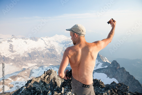 Mountain climber taking photo from summit of Ashlu Mountain in Coast Mountain Range, Squamish, British Columbia, Canada