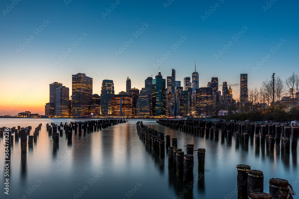 New York, USA - April 25, 2022: Long exposure of the Lower Manhattan skyline at sunset with an old Brooklyn pier in the foreground