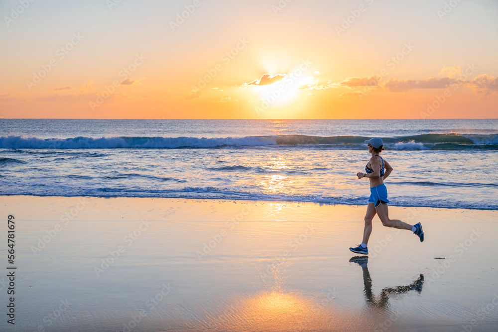 Woman jogging on beach at sunrise, Noosa Heads, Queensland, Australia Woman jogging on beach at sunrise, Noosa Heads, Queensland, Australia