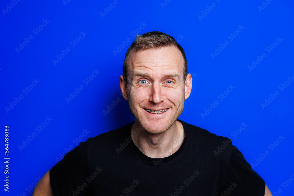 A young man in a black T-shirt on a blue background shows different emotions on his face. Cheerful man with a smile. Place for text. Male beauty A young man in a black T-shirt on a blue background shows different emotions on his face. Cheerful man with a smile. Place for text. Male beauty