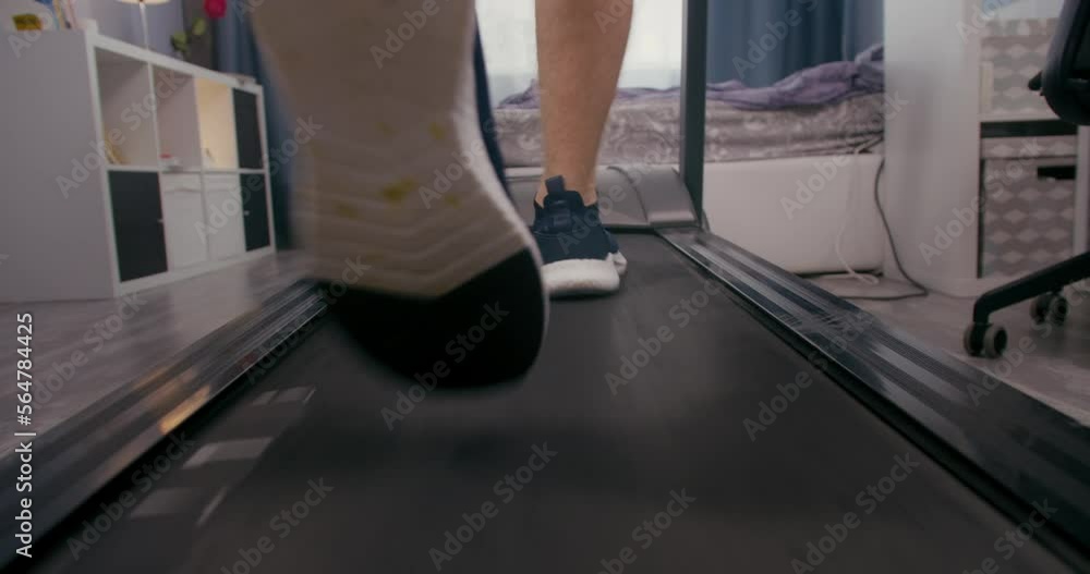 Foot running on treadmill at home. Back view of legs having workout on treadmill Foot running on treadmill at home. Back view of legs having workout on treadmill