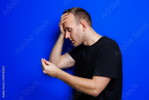 A young man in a black T-shirt on a blue background stands with a thermometer in his hands. An increase in body temperature, feeling sick. Weakened immunity. Selective focus