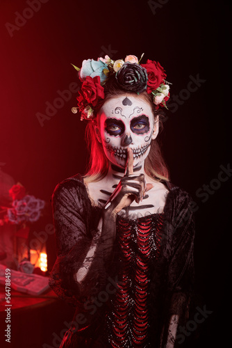 Creepy lady of death doing hush sign to keep secret, wearing santa muerte halloween costume and showing slience mute and secrecy gesture with finger over lips, holy dios de los muertos.