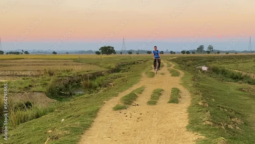 Village boy cycling on dirt road in Bangladesh farmlands, front view Village boy cycling on dirt road in Bangladesh farmlands, front view