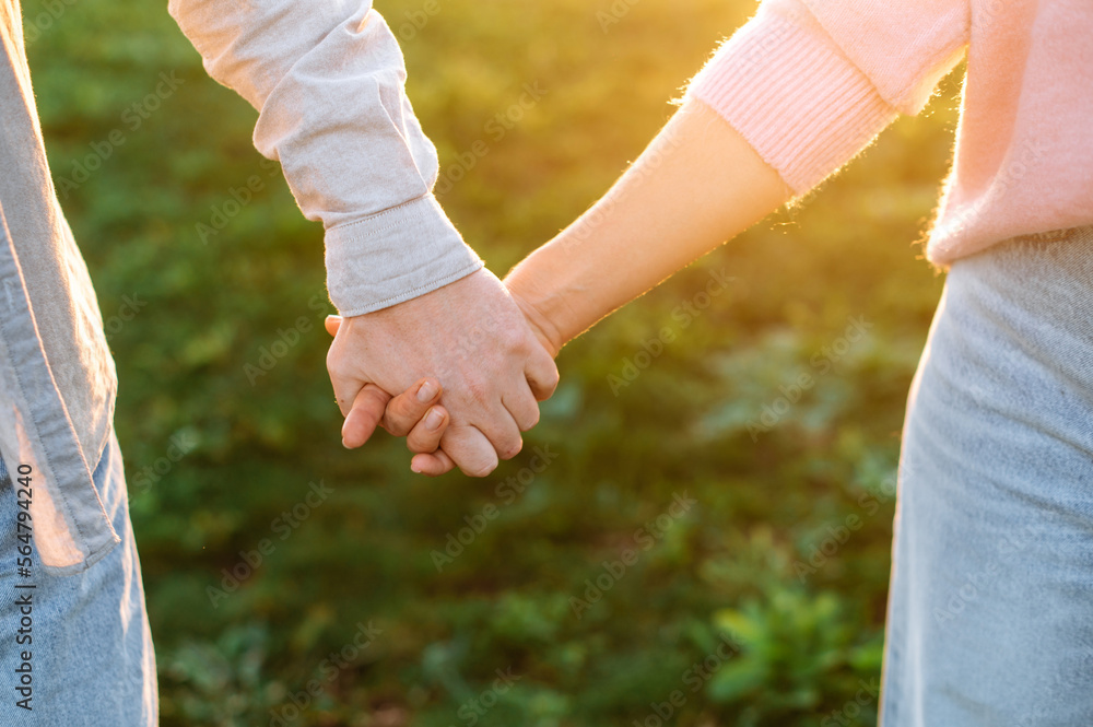 Close-up of the hands of a man and a woman caucasian nationality tenderly holding each other while walking outdoors at sunset. Tenderness and romantic feelings