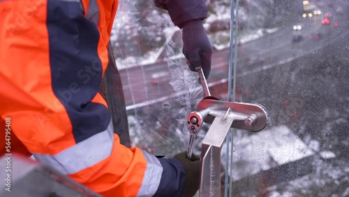 Close up of man hand in work glove tightening bolt with stainless steel wrench. Male worker using wrench tool while installing glass section on a bridge