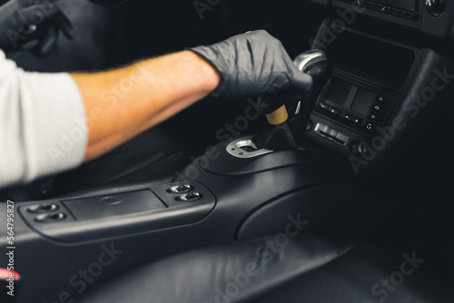 Unrecognisable man wearing black gloves wiping brush over gear shift of car. Car interior maintenance. Car detailing concept. Horizontal indoor shot. High quality photo