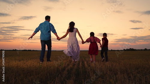 Parental care for children. Active family with children runs through a grassy field in the evening at sunset. Big family, group of people in nature. Son, Daughter, dad, mom, walk hand in hand outdoors