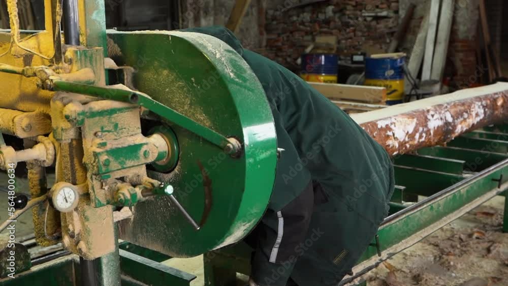 Mechanic repairs dirty bandsaw machine in sawmill for log sawing into planks Mechanic repairs dirty bandsaw machine in sawmill for log sawing into planks