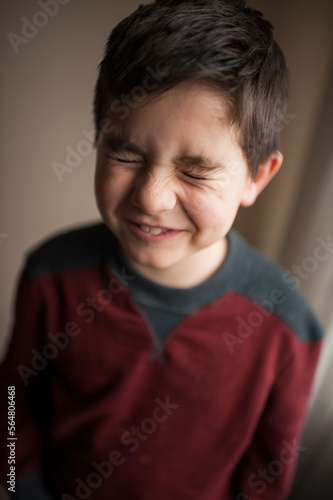 Cute portrait of young boy closing eyes tightly against neutral wall photo