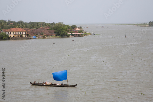 Small sailboat with blue tarp sail crosses waterway.