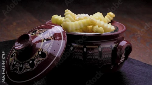 Shredding feta cheese over Bulgarian ceramic pot gyuveche filled with crinkle cut French fries. photo