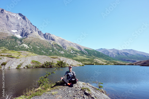 mature adult meditating in torres del paine national park with mountains and lake in the background © oscargutzo