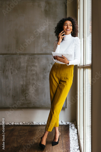 Cheerful woman with documents talking on smartphone
