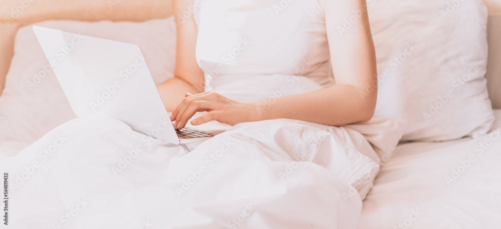 Lady working on a laptop in bed with white linens. Lady working on a laptop in bed with white linens.