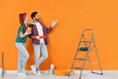 Happy designers with painting equipment near freshly painted orange wall indoors