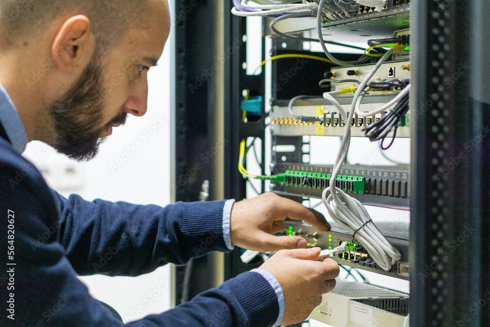 © ACALU Studio/Stocksy - Network engineer working in a telecom rack