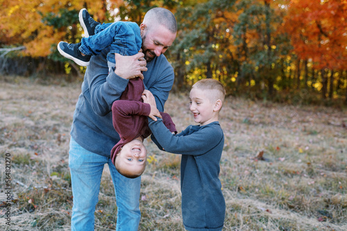 Father holding his son upside down and the brother tickles his tummy photo