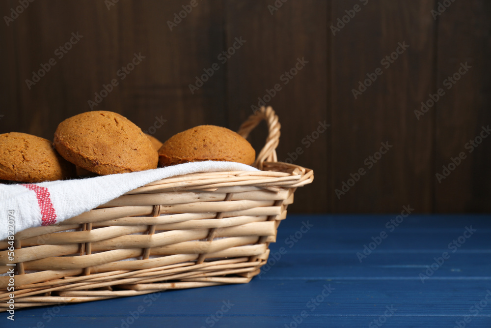 Wicker basket with tasty oatmeal cookies on blue wooden table. Space for text