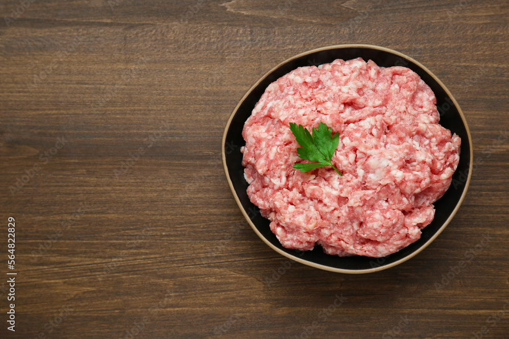 Bowl of raw fresh minced meat with parsley on wooden table, top view. Space for text Bowl of raw fresh minced meat with parsley on wooden table, top view. Space for text