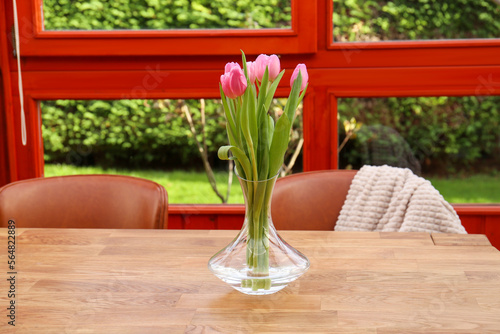 Pink tulips in glass vase on wooden table at terrace