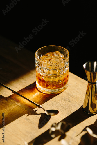 Canvas Print whisky drink on a wooden table with a barspoon and a jigger on black background