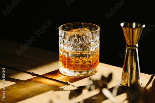 Bild auf Leinwand whiskey drink on a wooden table with a barspoon and a jigger on black background