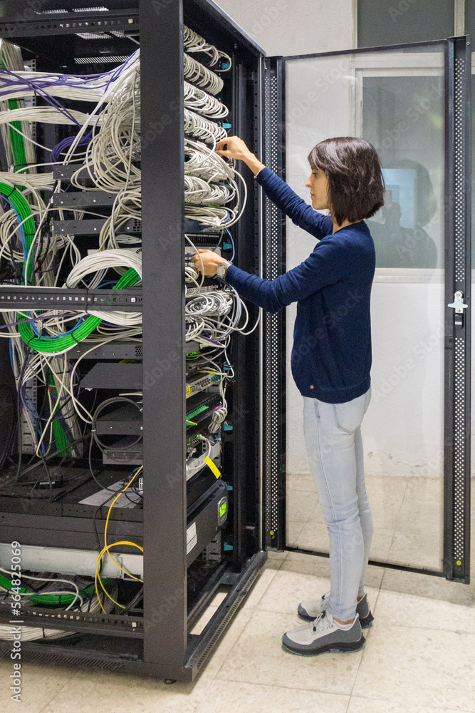 Computer technician woman connecting cables in a rack Computer technician woman connecting cables in a rack