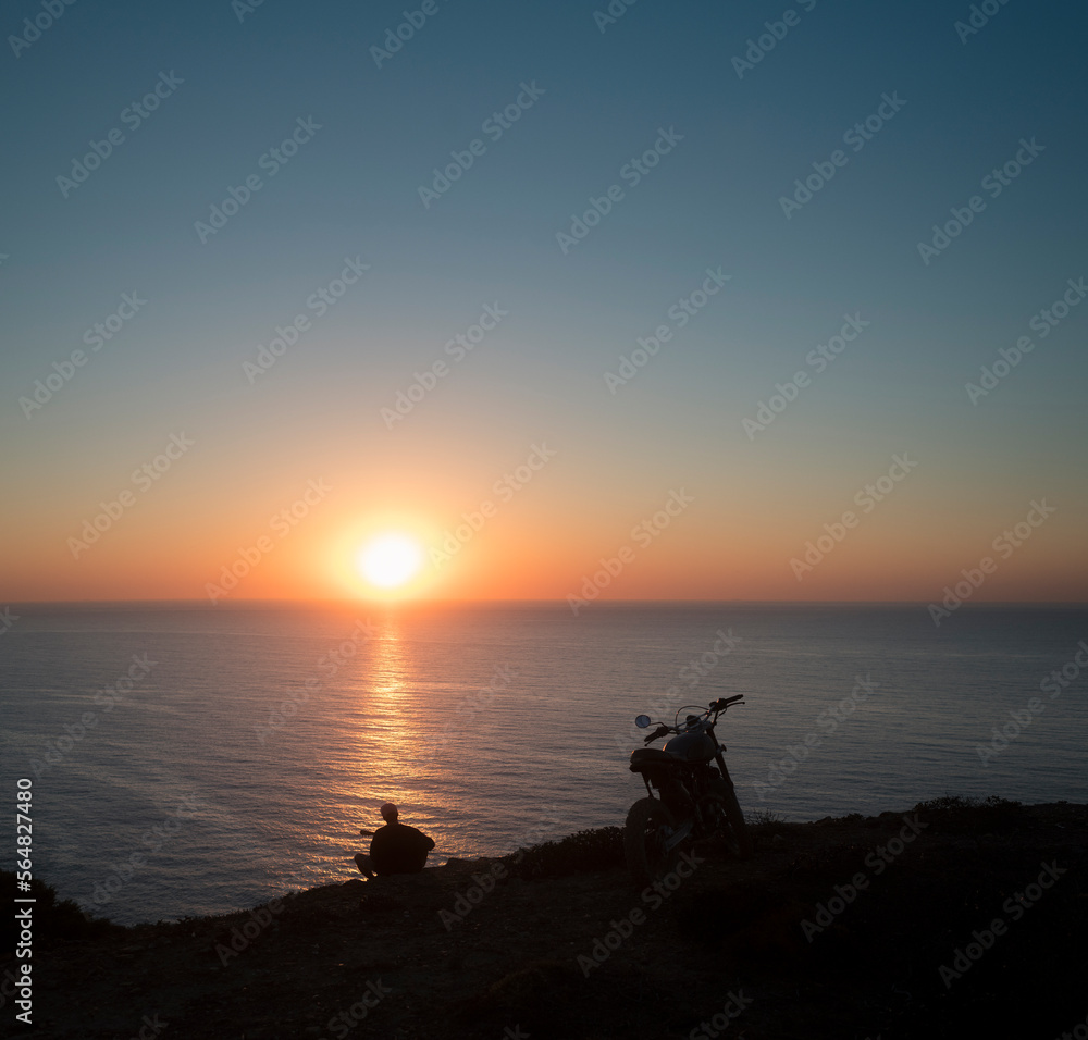 Man playing guitar with parked motorcycle at sunset cliff Man playing guitar with parked motorcycle at sunset cliff