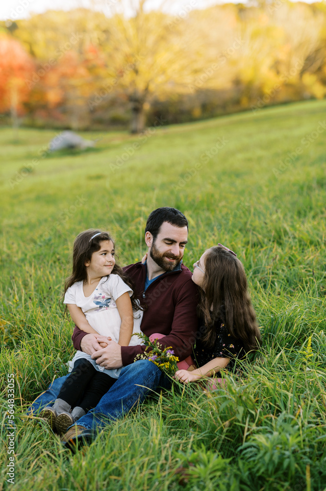 Two happy sisters sitting outdoors with their dad Two happy sisters sitting outdoors with their dad