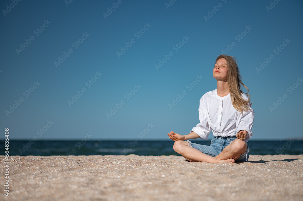 Girl meditating by the sea. Wind shakes long blond hair