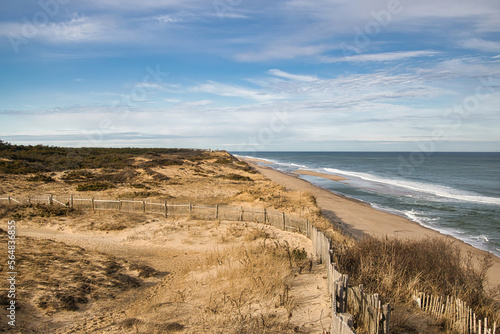 Under a partly cloudy blue sky on a snowless Winter day, the view of the ocean, beach and sand dunes at Marconi Beach, near Wellfleet, MA, on Cape Cod,