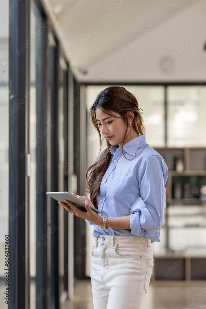 Young business Asian woman using tablet ipad, standing near the window in workplace Young business Asian woman using tablet ipad, standing near the window in workplace