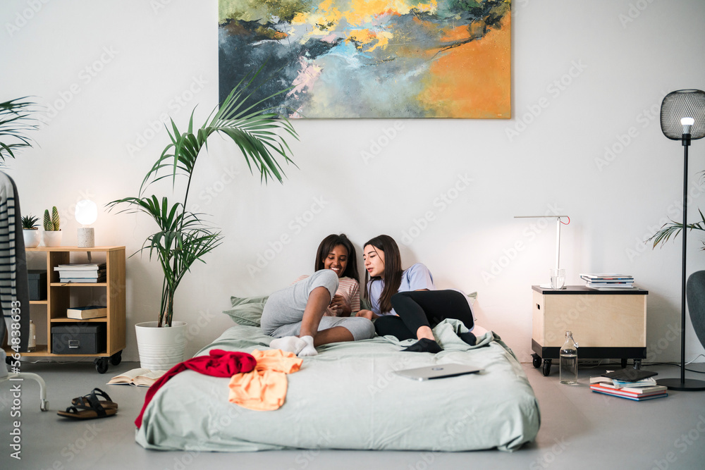 © Studio Marmellata/Stocksy - Happy young diverse ladies talking on bed at home