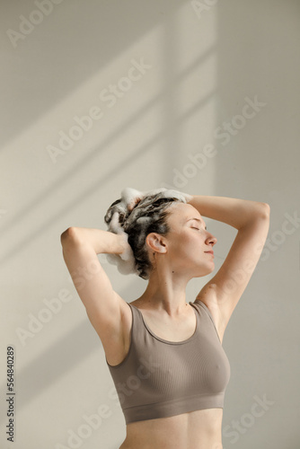 Young woman with hands touching her wet, soapy hair with shampoo foam photo