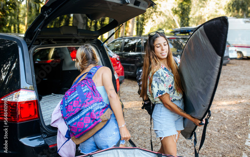 Female surfers taking belongings from car trunk