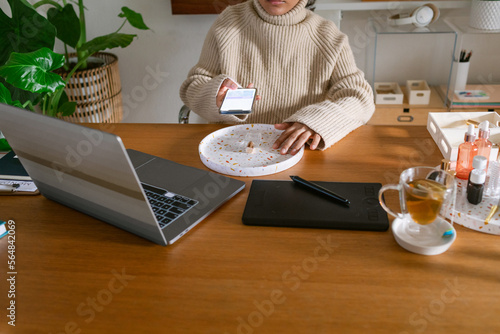 Woman using mobile camera taking product photo at desk