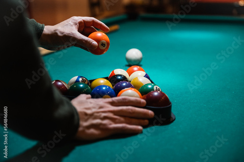 Crop man arranging balls in rack on billiard table photo