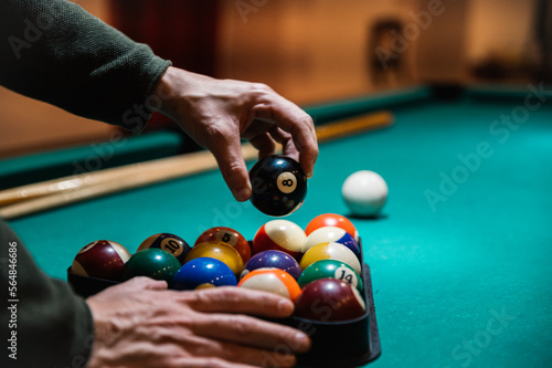 Crop man arranging balls in rack on billiard table