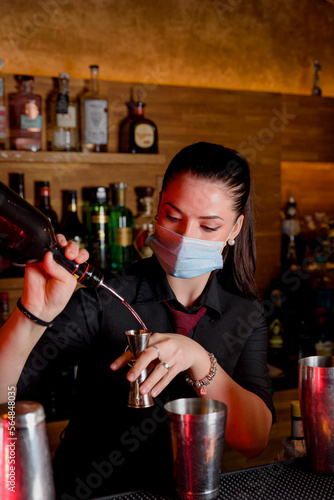 young woman bartender makes a cocktail with face mask