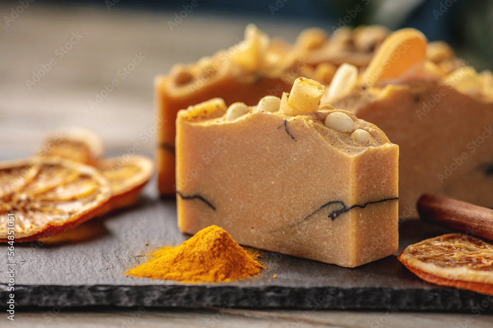Natural soap with slices of oranges and turmeric on the black and wooden background. Concept of making and using organic eco soap and cosmetics