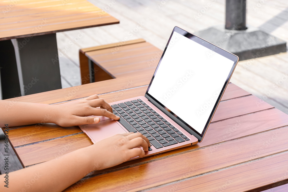 Little girl using laptop at table in street cafe, closeup Little girl using laptop at table in street cafe, closeup