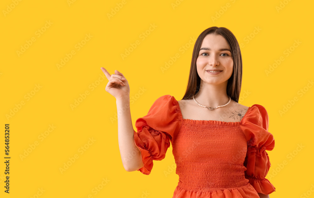 Young woman in stylish blouse pointing at something on yellow background Young woman in stylish blouse pointing at something on yellow background