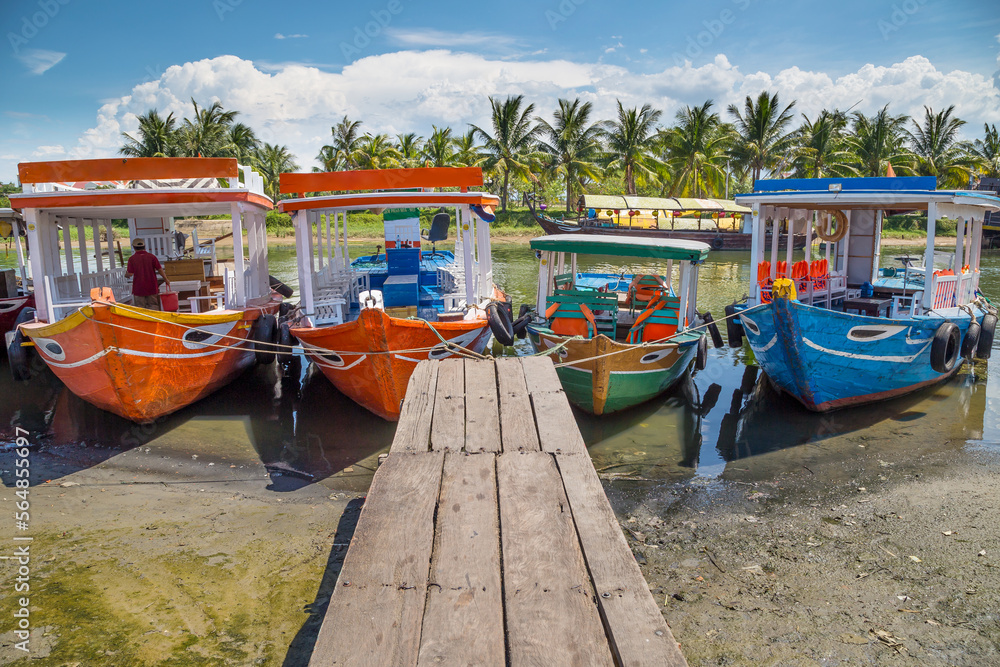 Four brightly painted tourist boats lined up on a river at the end of a wooden jetty at Hoi An in Vietnam