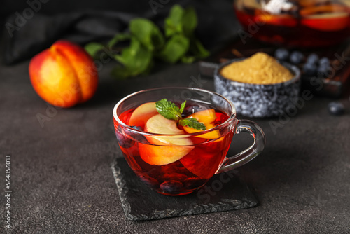 Glass cup of fruit tea with blueberries, apple and peach on dark background, closeup