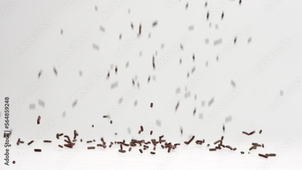 Brown chocolate sprinkles ice cream topping falling in slow motion and bouncing before settling into pile on white backdrop Brown chocolate sprinkles ice cream topping falling in slow motion and bouncing before settling into pile on white backdrop