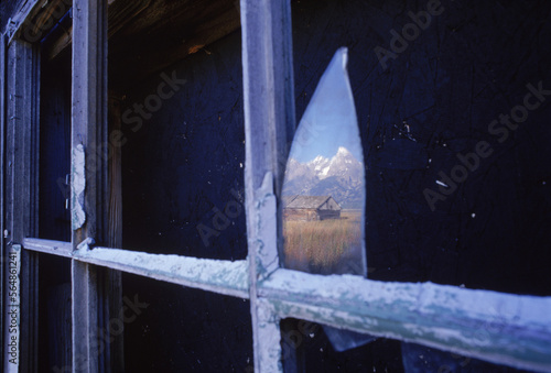 Mountain and sky reflection in a small shard of window glass in a broken cabin window frame near Jackson, Wyoming. photo