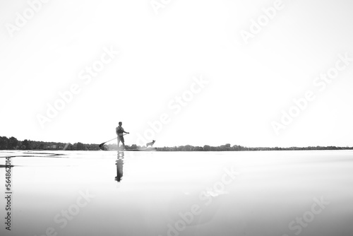 Black and white low angle perspective of a man stand up paddleboarding (SUP) with his dog against a blown out sky. photo