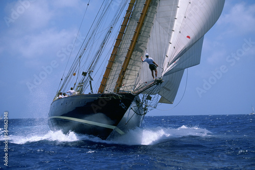 Man on bowsprit of wooden yacht.