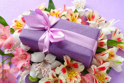 Beautiful composition with gift box and alstroemeria flowers on lilac background, closeup. Mother's day celebration